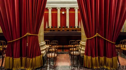 view of empty Supreme Court bench from back of courtroom with large curtains in foreground