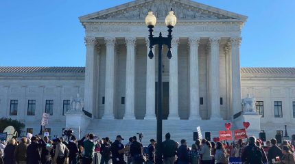 front of supreme court with crowd of people holding signs in foreground