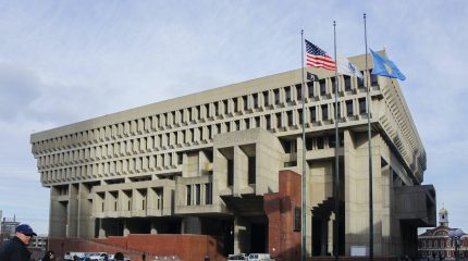 large cement building with three flagpoles in front