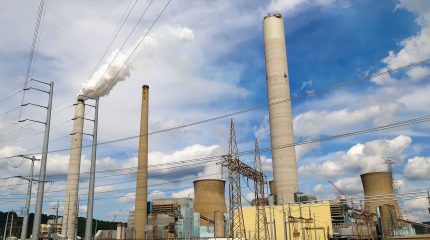 industrial facility with three tall smoke stacks and numerous power lines criss-crossing in foreground