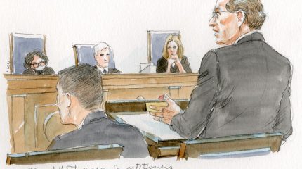 man in grey suit and glasses gestures as he argues at the lectern, in front of three seated justices