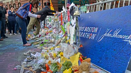 woman leaning over a street memorial of flowers, cards, and tennis shoes for the Boston Marathon bombing victims