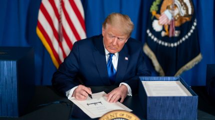 president trump sitting at desk and signing a document