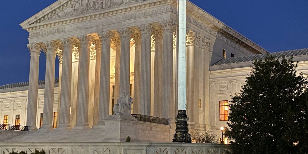 front of supreme court building illuminated against a dark sky