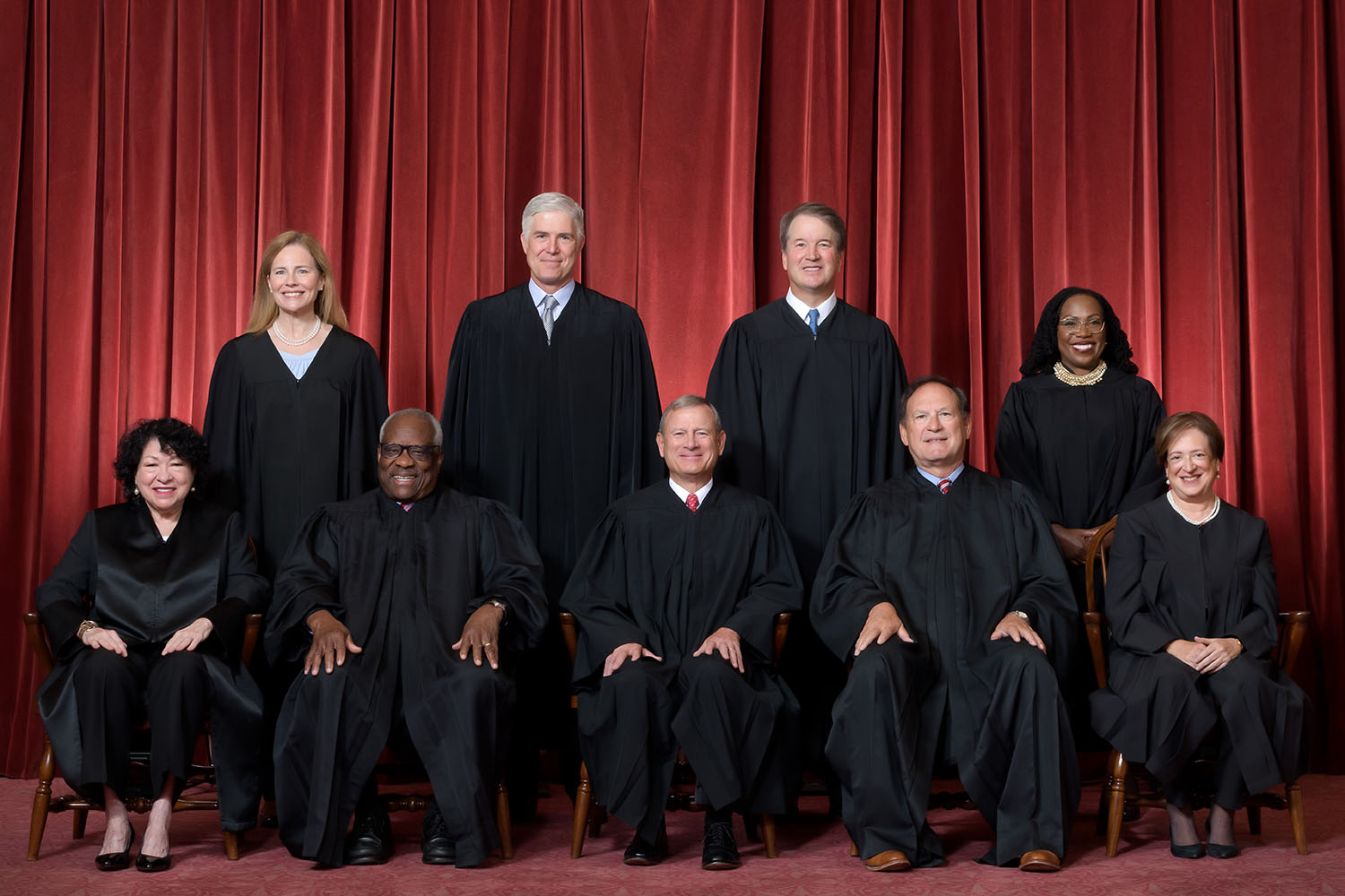 All nine justices pose in front of a red curtain