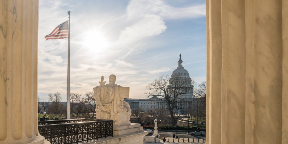 View of the US Capitol from the United States Supreme Court in Washington, DC with blue sky and US flag