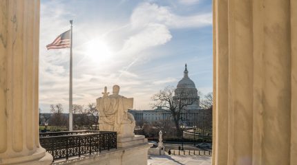 View of the US Capitol from the United States Supreme Court in Washington, DC with blue sky and US flag