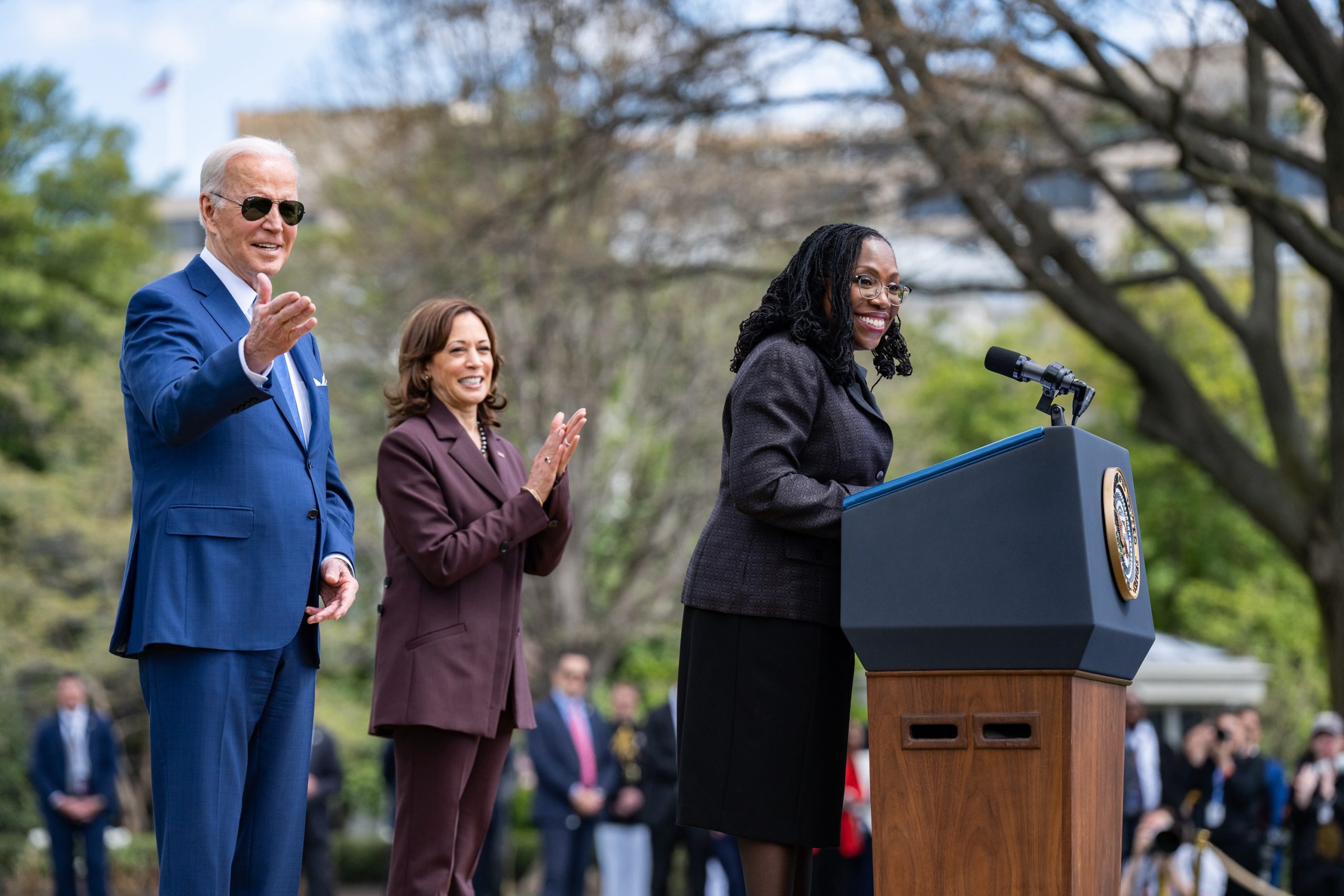 Justice Jackson speaks at lectern, President Biden and Vice President Harris stand behind her.