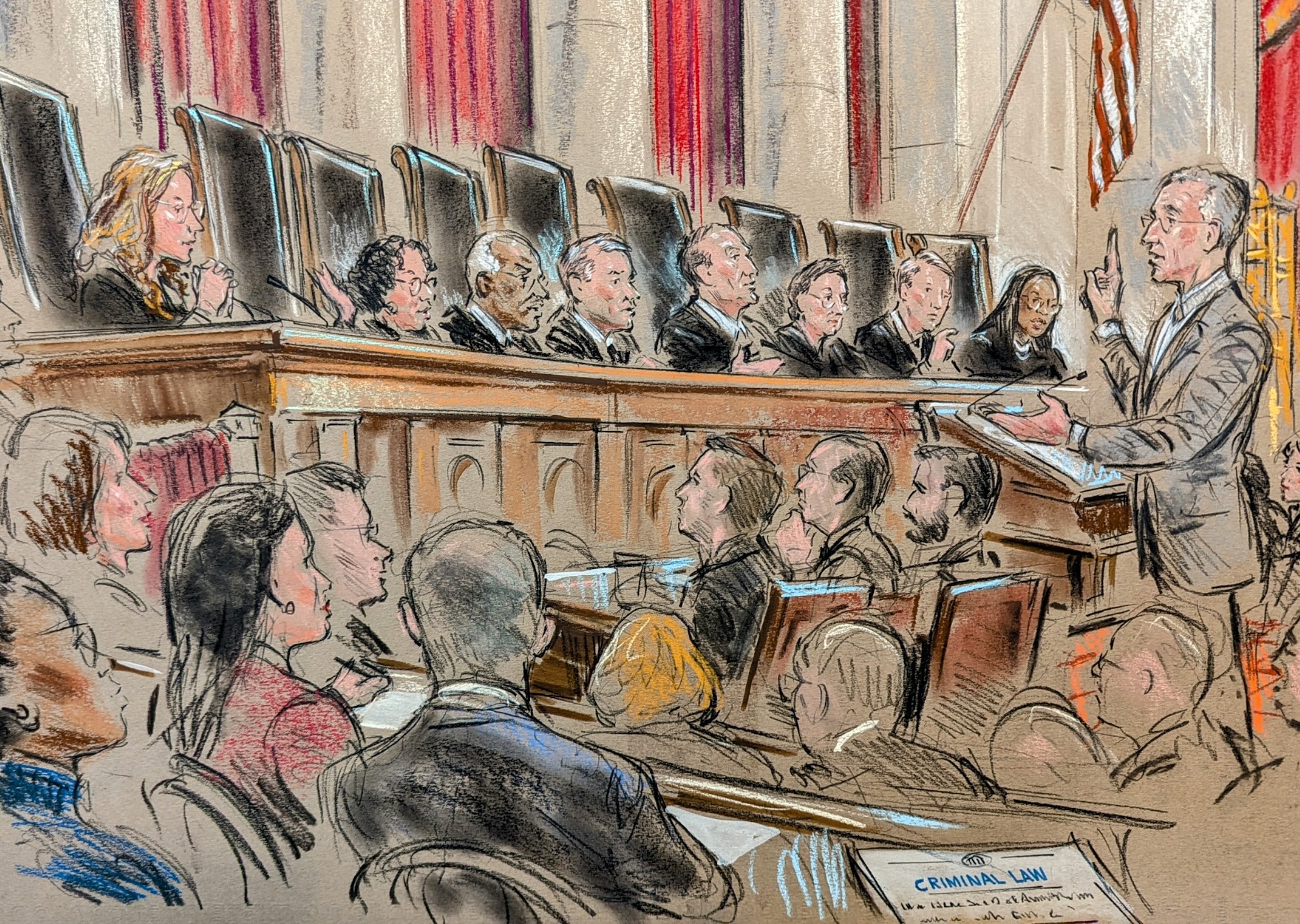 Man speaks to justices on bench while crowd looks on.